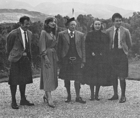 Photo of a family, as adults standing on gravel with hills in the background
    