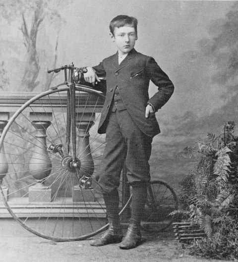 Photo of a boy standing beside a penny farthing bicycle
    